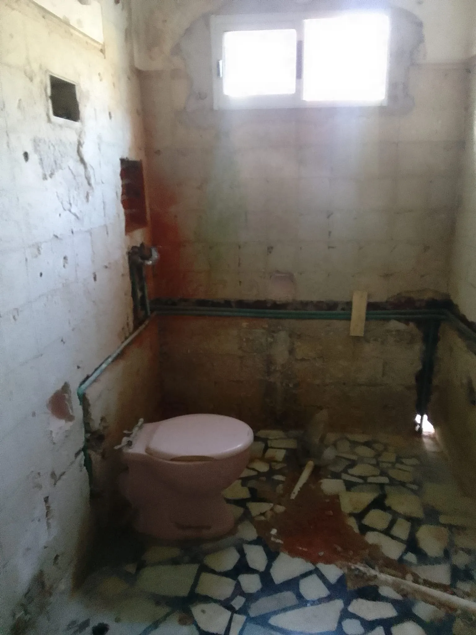 Baño antes de la reforma, con paredes desconchadas y suelo roto