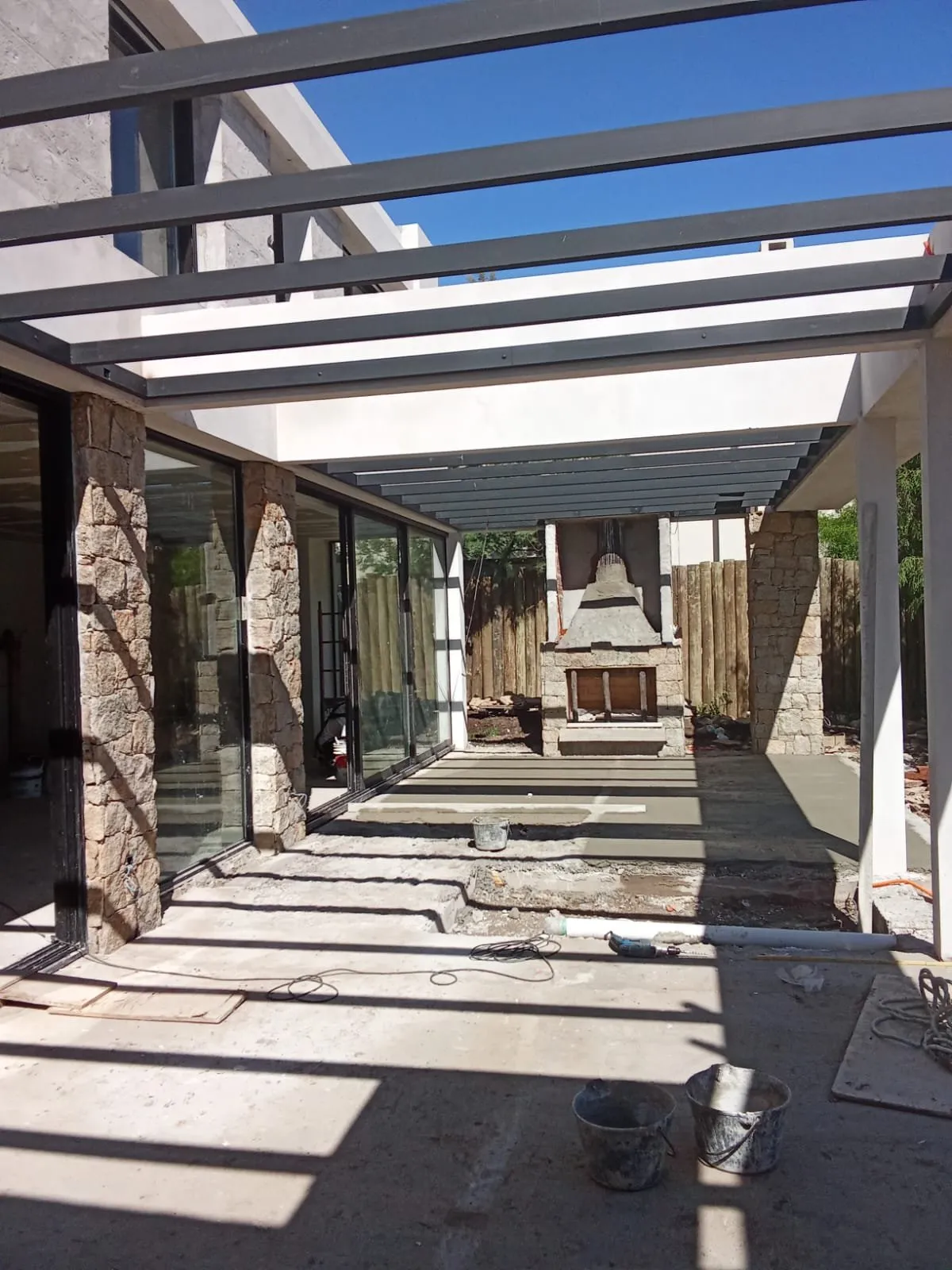 Porche con pérgola metálica y muros de piedra durante la obra